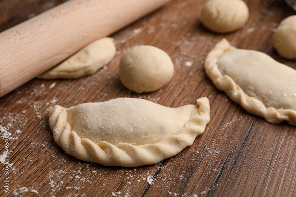 Uncooked chebureki, dough and rolling pin on wooden table Uncooked chebureki, dough and rolling pin on wooden table