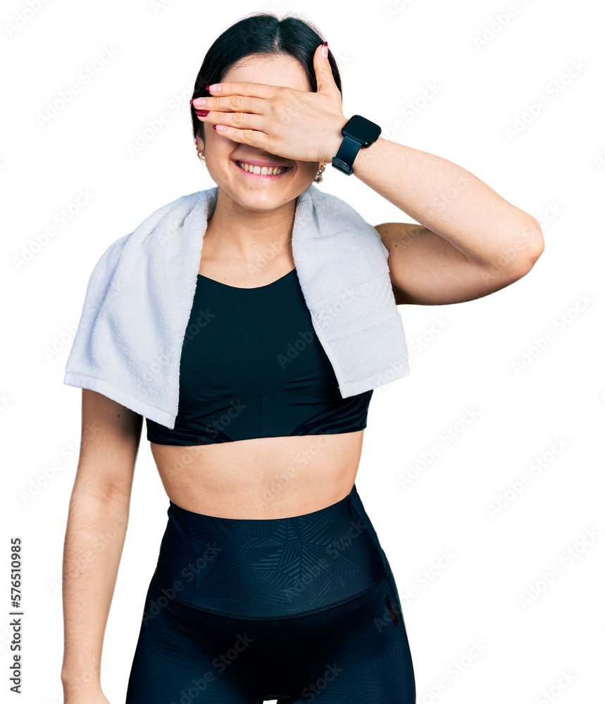 Young brunette woman with blue eyes wearing sportswear and towel smiling and laughing with hand on face covering eyes for surprise. blind concept. Young brunette woman with blue eyes wearing sportswear and towel smiling and laughing with hand on face covering eyes for surprise. blind concept.