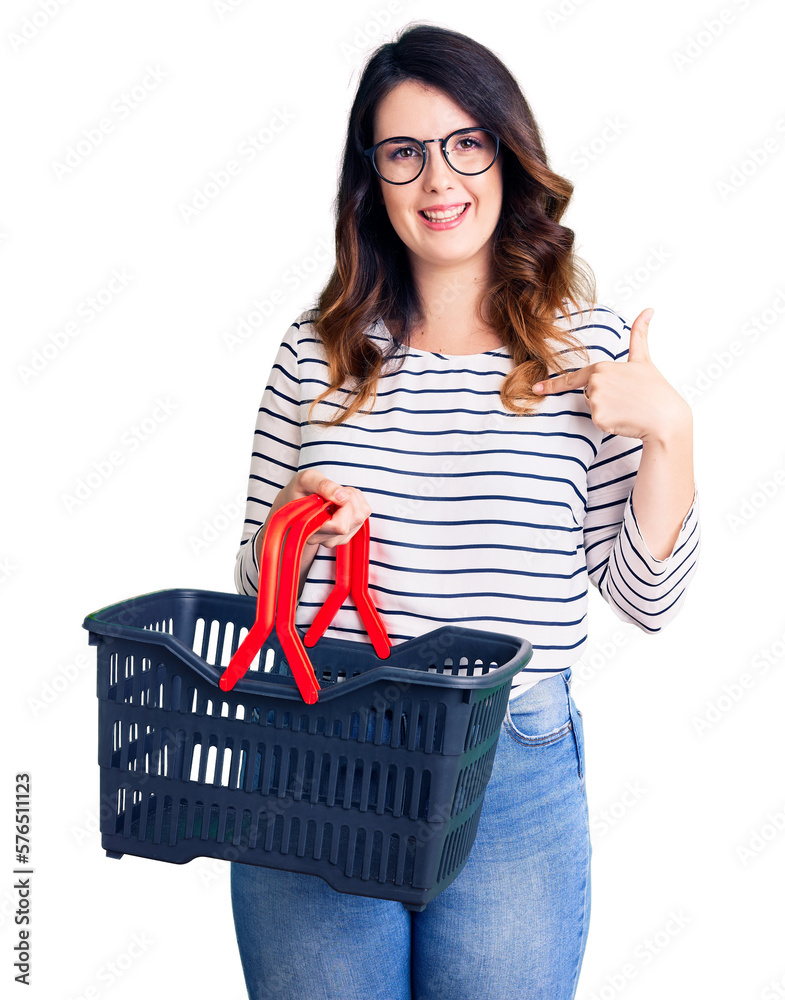 Beautiful young brunette woman holding supermarket shopping basket pointing finger to one self smiling happy and proud Beautiful young brunette woman holding supermarket shopping basket pointing finger to one self smiling happy and proud