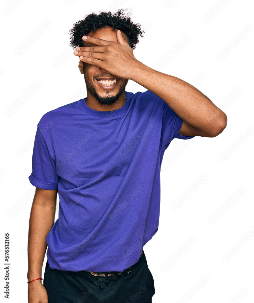 Young african american man with beard wearing casual purple t shirt smiling and laughing with hand on face covering eyes for surprise. blind concept. Young african american man with beard wearing casual purple t shirt smiling and laughing with hand on face covering eyes for surprise. blind concept.