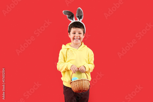 Cute little boy with bunny ears and Easter basket on red background