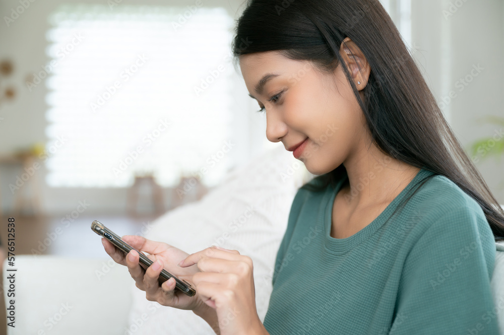 Happy young asian woman relaxing at home she is sitting on sofa and using mobile smartphone Happy young asian woman relaxing at home she is sitting on sofa and using mobile smartphone