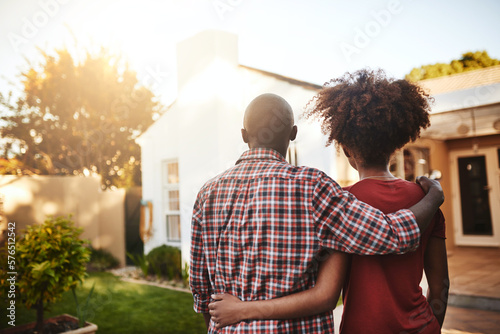 What a lovely place to call our home. Rear view shot of a young couple admiring their new house outside.