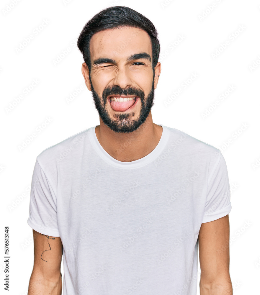 Young hispanic man wearing casual white t shirt winking looking at the camera with sexy expression, cheerful and happy face. Young hispanic man wearing casual white t shirt winking looking at the camera with sexy expression, cheerful and happy face.
