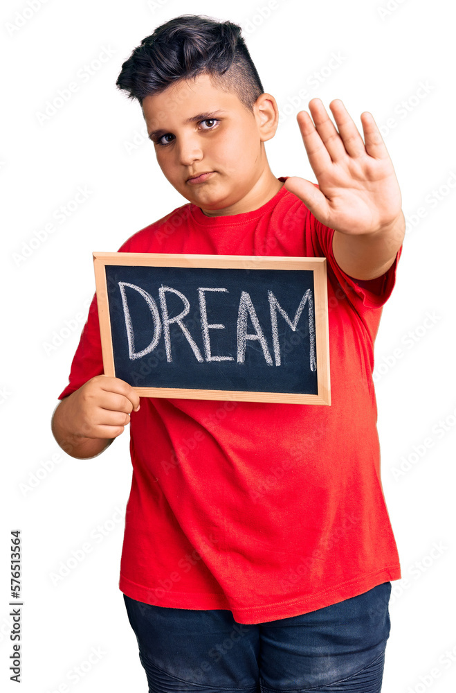 Little boy kid holding blackboard with dream word with open hand doing stop sign with serious and confident expression, defense gesture Little boy kid holding blackboard with dream word with open hand doing stop sign with serious and confident expression, defense gesture