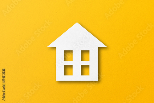 White paper cut out house shape isolated on yellow paper background.