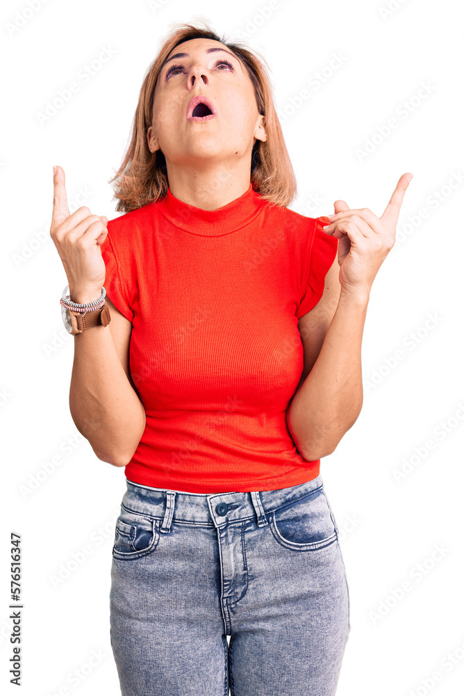 Young blonde woman wearing casual clothes amazed and surprised looking up and pointing with fingers and raised arms. Young blonde woman wearing casual clothes amazed and surprised looking up and pointing with fingers and raised arms.