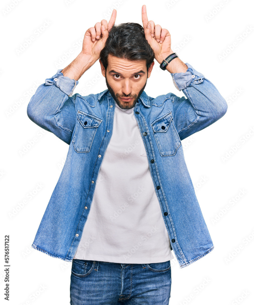 Young hispanic man wearing casual clothes doing funny gesture with finger over head as bull horns Young hispanic man wearing casual clothes doing funny gesture with finger over head as bull horns