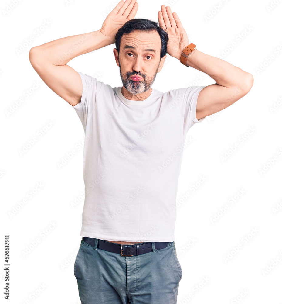 Middle age handsome man wearing casual t-shirt doing bunny ears gesture with hands palms looking cynical and skeptical. easter rabbit concept. Middle age handsome man wearing casual t-shirt doing bunny ears gesture with hands palms looking cynical and skeptical. easter rabbit concept.