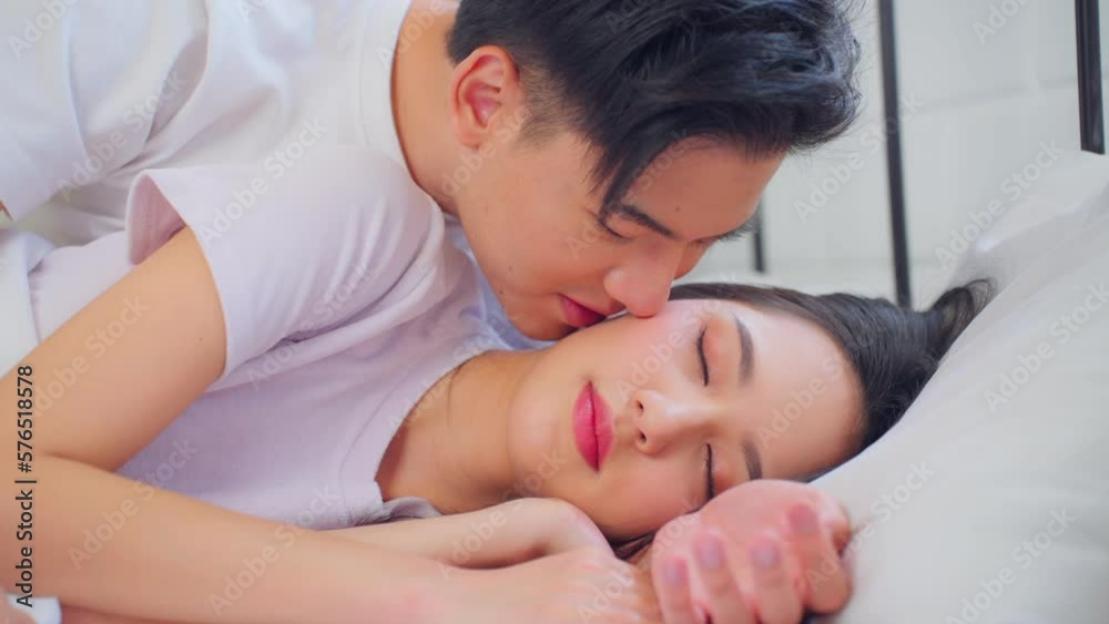Asian husband kissing his wife while lying down sleep on bed in bedroom Asian husband kissing his wife while lying down sleep on bed in bedroom