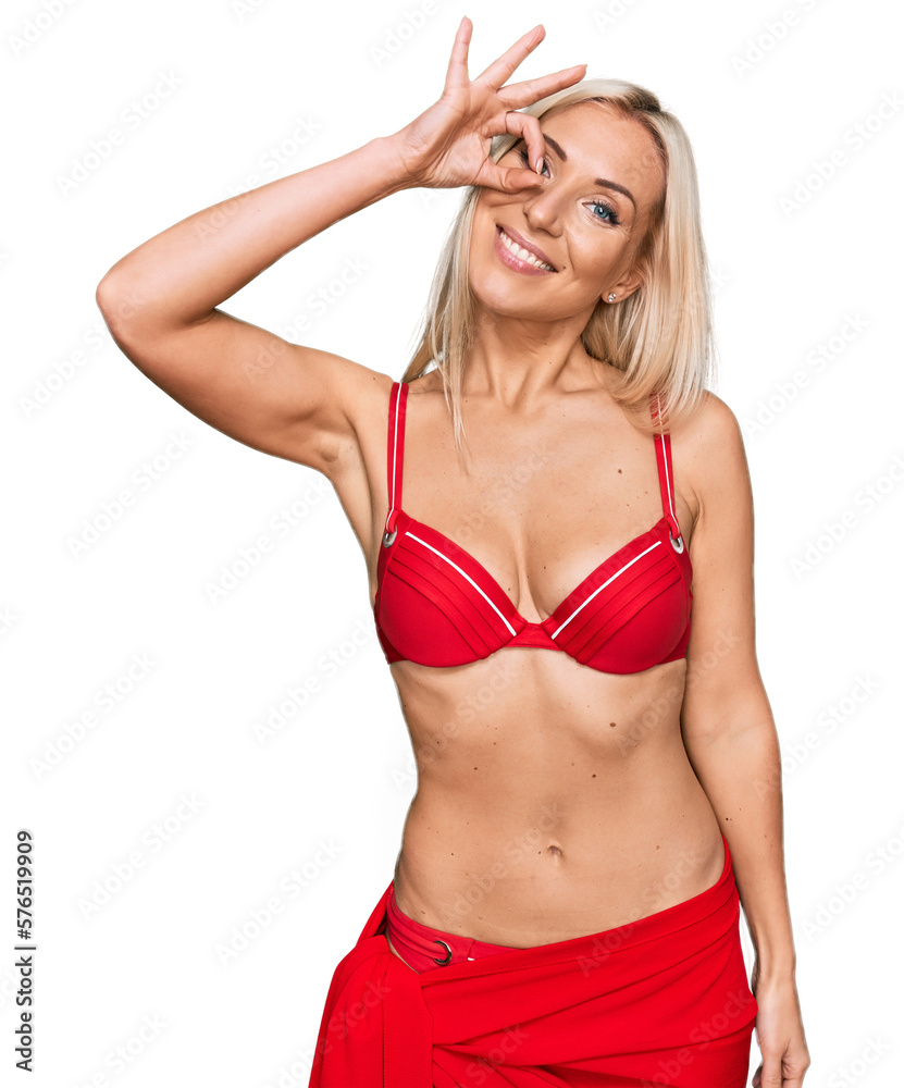 Young blonde woman wearing bikini smiling happy doing ok sign with hand on eye looking through fingers Young blonde woman wearing bikini smiling happy doing ok sign with hand on eye looking through fingers