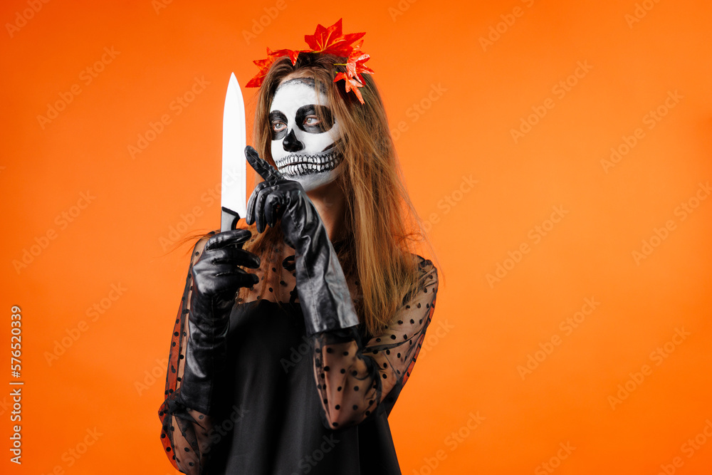 happy woman in traditional day of dead makeup touching black veil and looking at camera isolated on orange