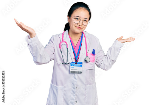 Young chinese woman wearing doctor uniform and stethoscope clueless and confused expression with arms and hands raised. doubt concept.