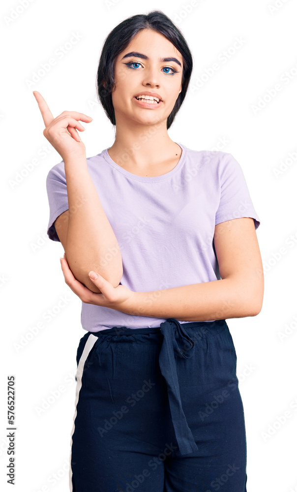 Brunette teenager girl wearing casual clothes with a big smile on face, pointing with hand and finger to the side looking at the camera.