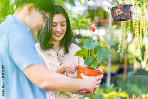 Happy Adult Asian family couple choosing and buying plant together at plant shop street market on summer vacation. Man and woman enjoy hobbies and leisure activity growing plant and flower at home.