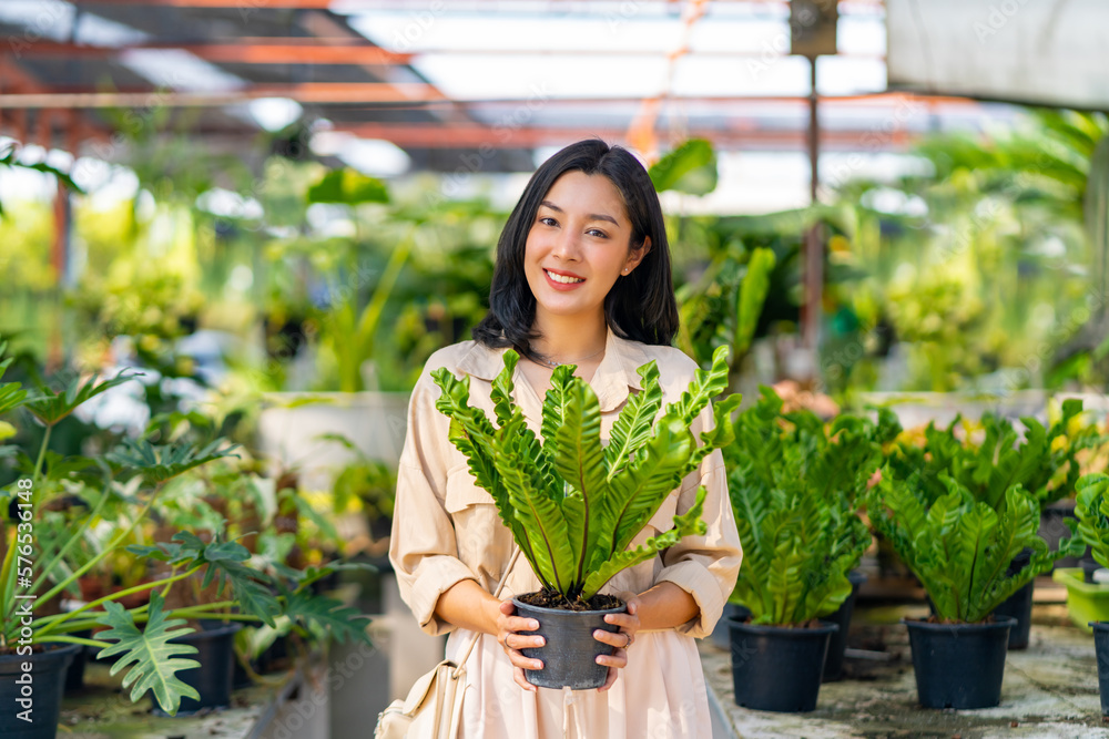 Portrait of Happy Asian woman holding potted plant in front of plant ...