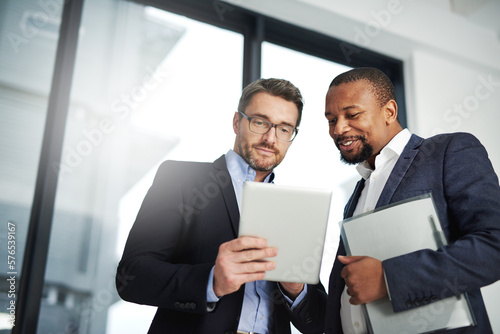 Interactive collaborations with the help of wireless technology. Shot of two businessmen using a digital tablet together at work.