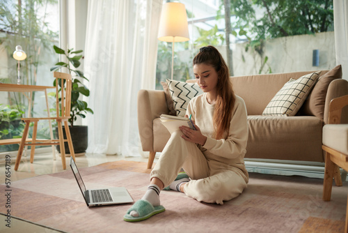Фотография Girl sitting on floor at home and filling gratitude journal