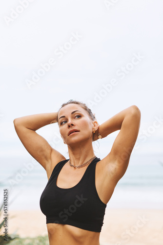 Beautiful girl taking break during yoga exercises, collecting curly dark hair in front of sea