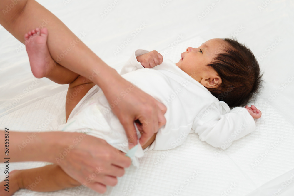 mother changing diaper of newborn baby while lying on bed