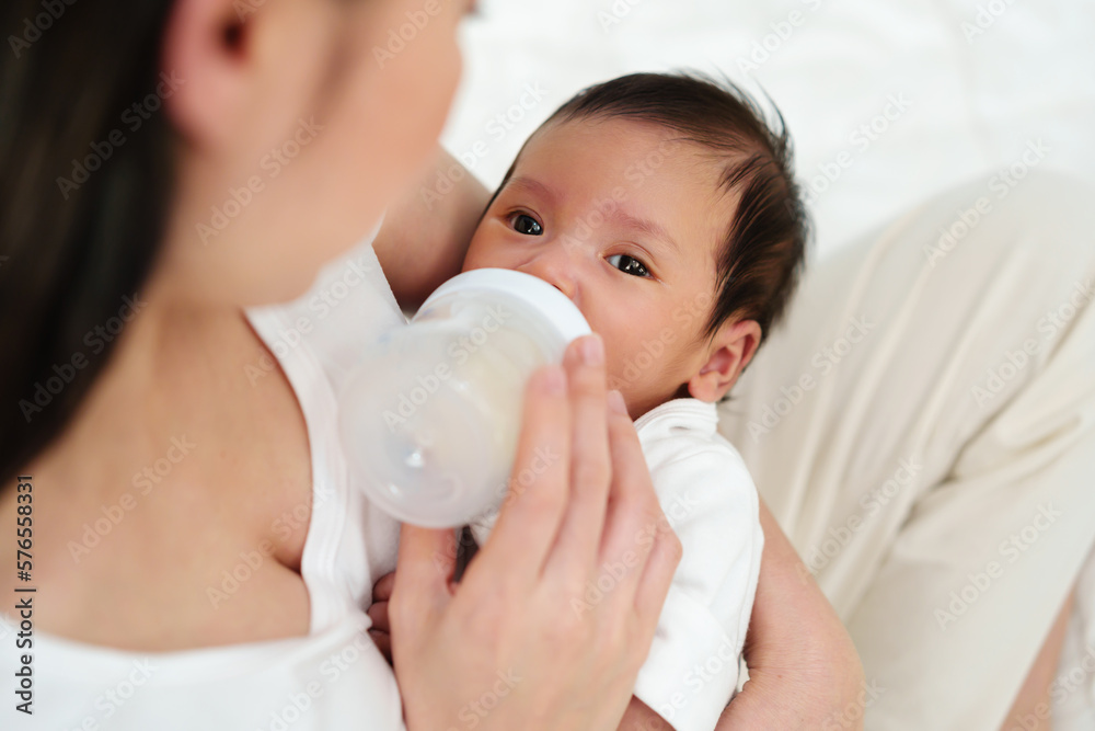 mother feeding milk bottle to her newborn baby on bed mother feeding milk bottle to her newborn baby on bed