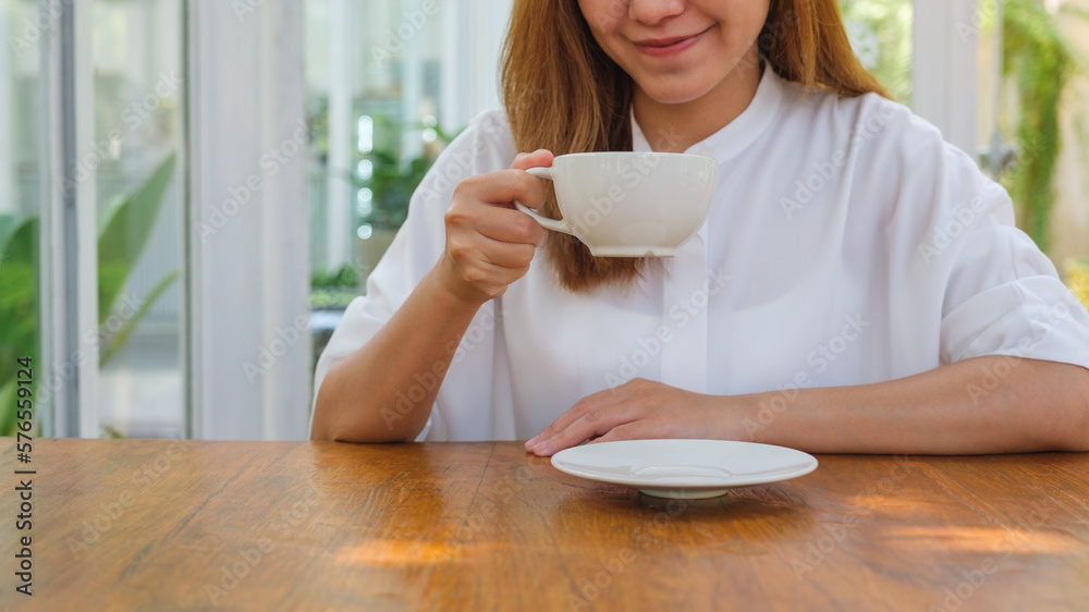 Closeup image of a young woman holding and drinking hot coffee in cafe Closeup image of a young woman holding and drinking hot coffee in cafe