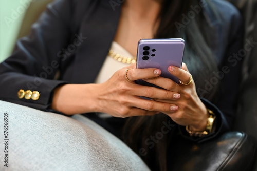 Cropped image of businesswoman in stylish suit using smart phone while sitting on couch.