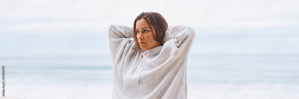 Attractive young woman in white hoodie walking along the seashore early morning Attractive young woman in white hoodie walking along the seashore early morning