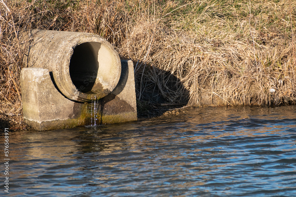 Drainage pipe made of concrete leaking water into pond Stock Photo