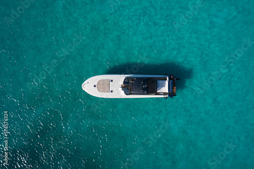 Big white motor boat anchored on the blue sea top view. White modern boat with motor on blue transparent water aerial view.
