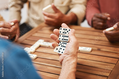 Hands, dominoes and friends in board games on wooden table for fun activity, social bonding or gathering. Hand of domino player holding rectangle number blocks playing with group for entertainment photo