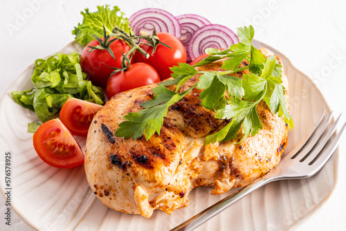 grilled chicken breasts on a white ceramics plate serving with parsley, tomato slices. close-up. diet food.