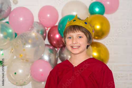 a happy boy with a crown on his head stands in front of a brick wall decorated with balloons © Ruslan Russland