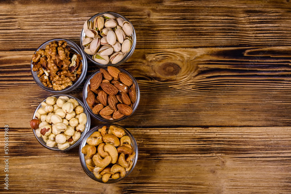Various nuts (almond, cashew, hazelnut, pistachio, walnut) in glass bowls on a wooden table. Vegetarian meal. Healthy eating concept. Top view Various nuts (almond, cashew, hazelnut, pistachio, walnut) in glass bowls on a wooden table. Vegetarian meal. Healthy eating concept. Top view