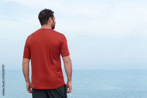 Rear view of a male sport person looking at the sea after training. 