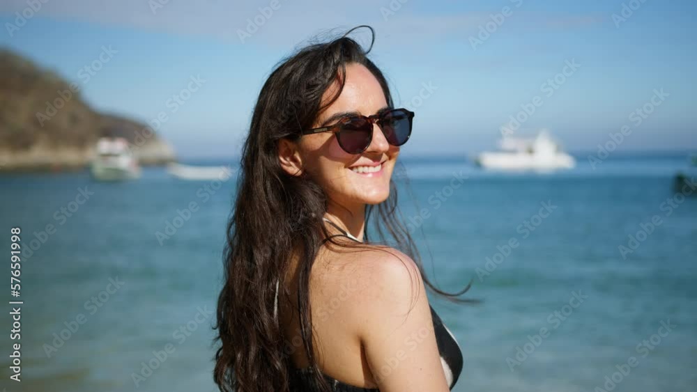 Smiling young woman is in front of the sea and look at the camera