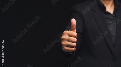 Businessman in a suit showing thumbs up while standing on a black background in the office