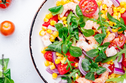 Delicious shrimp salad with sweet corn, cherry tomatoes, lamb lettuce and red onion on white table background. Top view