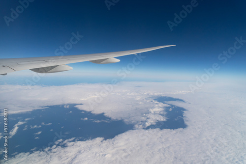 Wing of an airplane jet flying above clouds with blue sky from the window in traveling and transportation concept. Nature landscape background.