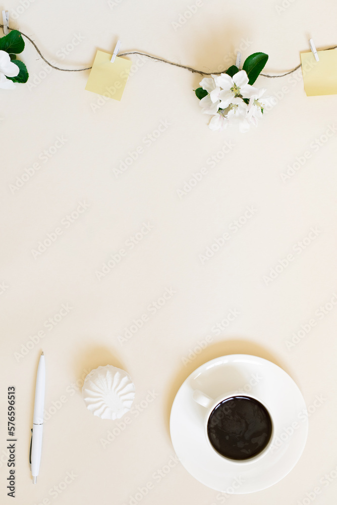 White apple blossoms suspended on a string with wooden clothespins and pieces of paper for notes, a cup of coffee, a pen and marshmallows on a beige background. Workplace of a female blogger White apple blossoms suspended on a string with wooden clothespins and pieces of paper for notes, a cup of coffee, a pen and marshmallows on a beige background. Workplace of a female blogger