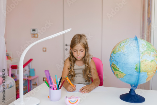 Girl sits at home at a table and write in a notebook, completing a learning task or repeating lessons at home