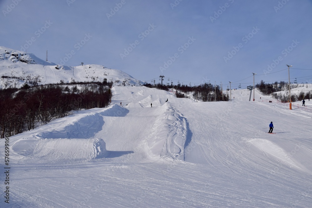Hovden, Norway, February 23, 2023. Hovden Alpinsenter, ski resort with ski slopes. Mountain with snow and trees, people skiing and snowboarding. Bluebird Weather. 
