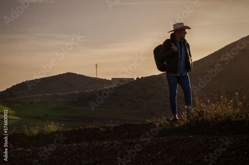 Adult man on cowboy hat standing on hill against mountain during sunrise