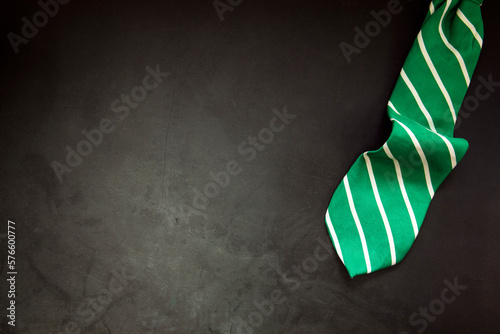 stylish tied green striped tie on dark concrete background top view, copy space, men,business,meeting,party concept