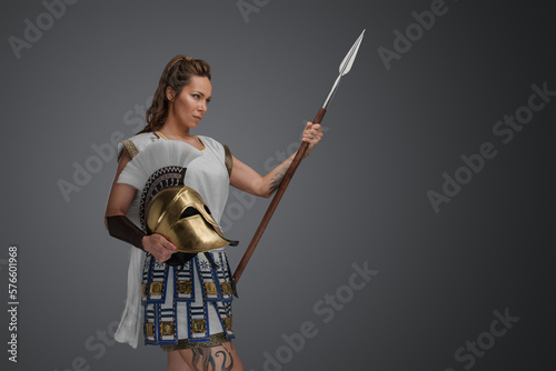 Shot of determined greek soldier woman dressed in armor and holding spear with helmet.