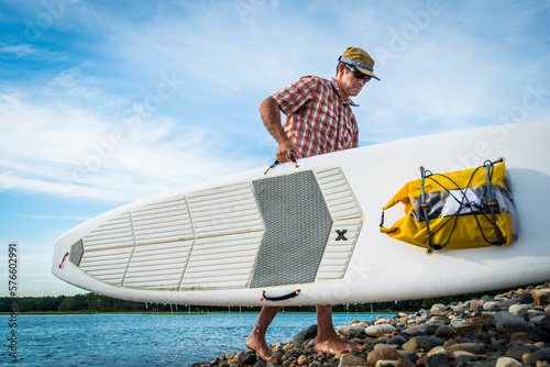 Paddleboarder carrying surfboard on rocky shore, Kittery, Maine, USA photo