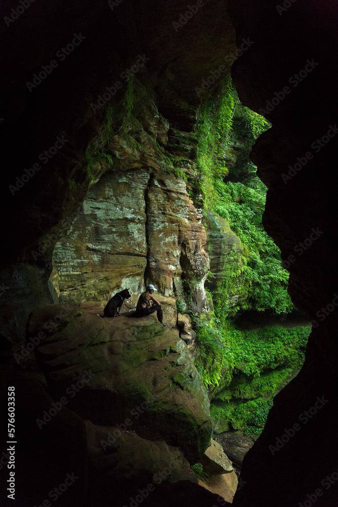 Woman with dog sitting on cliff in cave, Athens, Ohio, USA Woman with dog sitting on cliff in cave, Athens, Ohio, USA