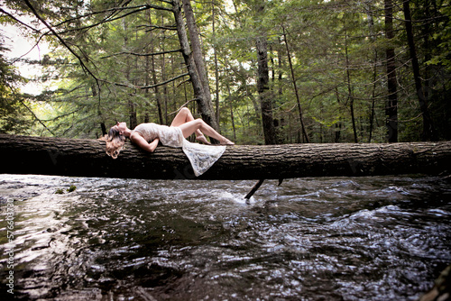 A woman in a white dress lays on a log across a river