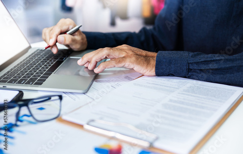 Focused financier accountant on paper work on desk office, asian businessman using laptop for review reports of investment and summary reports via online meeting with his business group