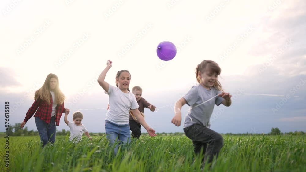 Kids are having fun playing in backyard. Happy family runs with balloons in park. Cheerful smile of children playing in park in nature. Freedom in summer group of children run together with balloons Kids are having fun playing in backyard. Happy family runs with balloons in park. Cheerful smile of children playing in park in nature. Freedom in summer group of children run together with balloons